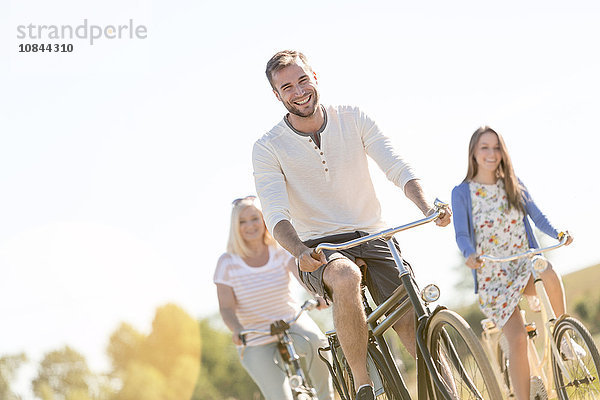 Lächelnder junger Mann beim Radfahren mit Frauen