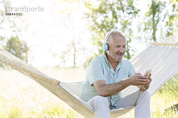 Senior Mann mit Kopfhörer Musik hören mit mp3-Player auf Sommer-Hängematte