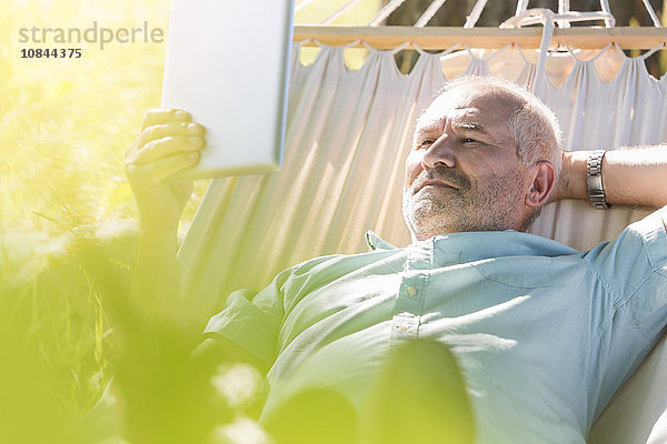 Senioren-Mann mit Digital-Tablett und Entspannung in der Sommer-Hängematte