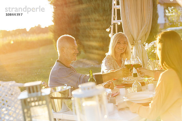 Senior Paar eine erwachsene Tochter Toasting Weingläser an der sonnigen Terrasse Tisch