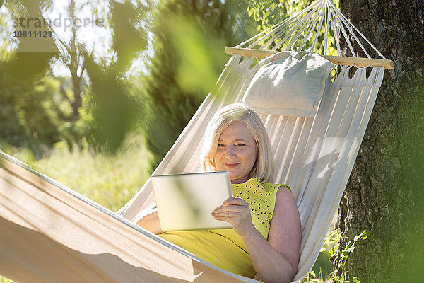 Seniorin mit digitalem Tablett und Entspannung in der Sommerhängematte
