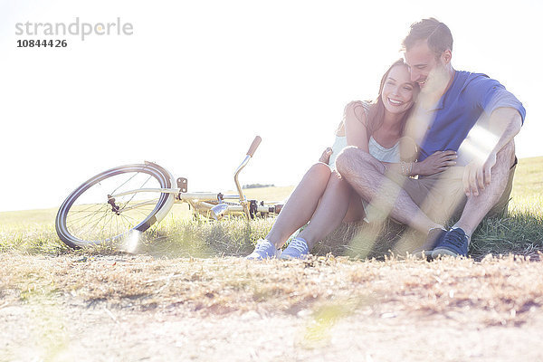 Zärtliches junges Paar  das sich in der Nähe des Fahrrads in ländlichem Gras umarmt