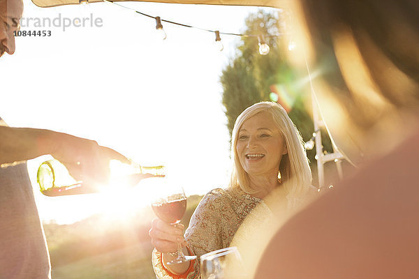 Älterer Mann  der Wein für seine Frau auf der sonnigen Terrasse gießt