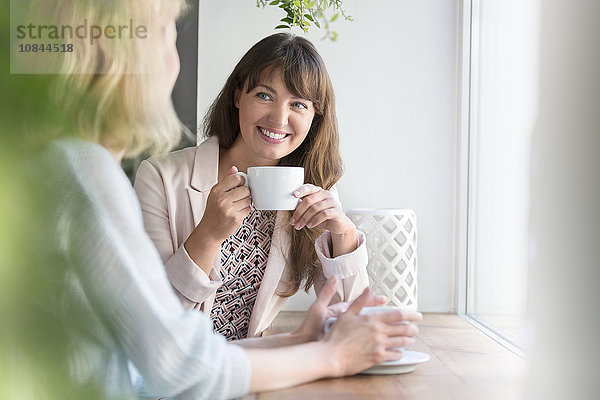 Lächelnde Frauen beim Kaffeetrinken am Caféfenster