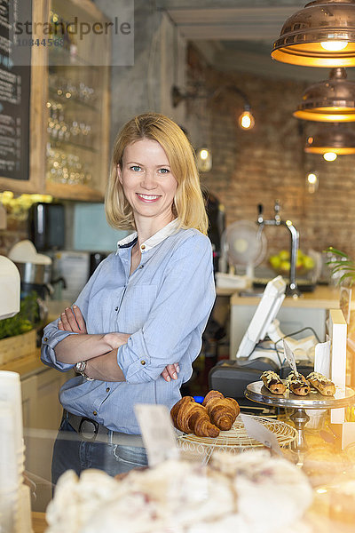 Portrait lächelnder Cafébesitzer mit gekreuzten Armen hinter der Theke