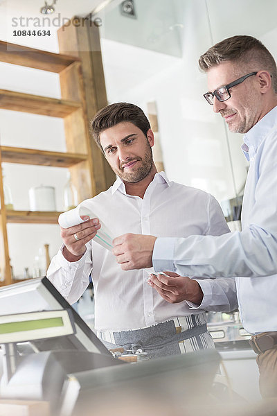 Kaffeehausbesitzer und Kellner bei der Überprüfung der Quittung an der Kasse