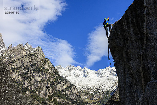 Kletterer an steiler Felswand  im Hintergrund blauer Himmel und schneebedeckte Gipfel der Alpen  Masino-Tal  Valtellina  Lombardei  Italien  Europa