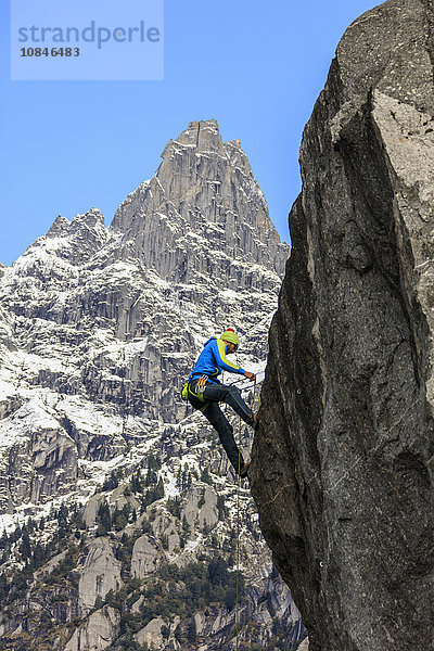 Kletterer an steiler Felswand  im Hintergrund blauer Himmel und Gipfel der Alpen  Masino-Tal  Valtellina  Lombardei  Italien  Europa