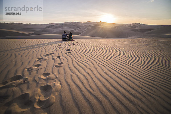 Paar beobachtet den Sonnenuntergang über Sanddünen in der Wüste von Huacachina  Region Ica  Peru  Südamerika
