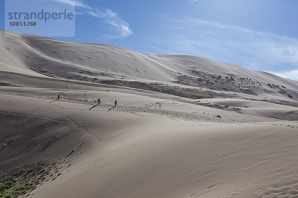 Entfernte Menschen  die eine riesige Sanddüne hinabsteigen  schillernd an einem Sommerabend  Khongoryn Els  Wüste Gobi  Mongolei  Zentralasien  Asien