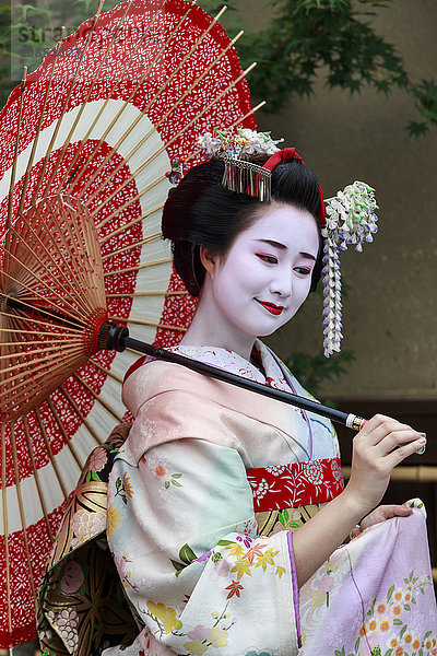 Porträt einer lächelnden Geisha in geblümten Gewändern mit rotem Regenschirm im Sommer  Kyoto  Japan  Asien