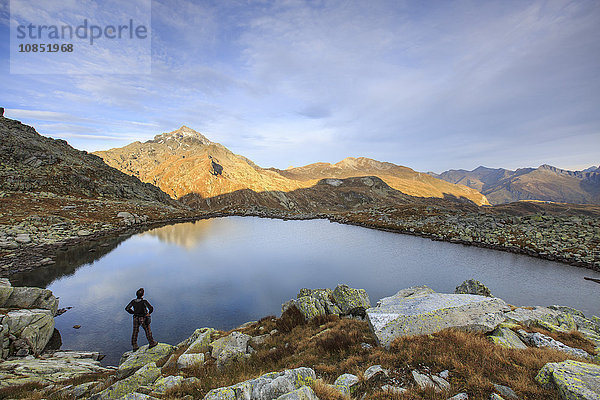 Wanderer bewundert den Bergsee bei Sonnenaufgang  Chiavenna Valle  Splugatal  Schweiz  Europa