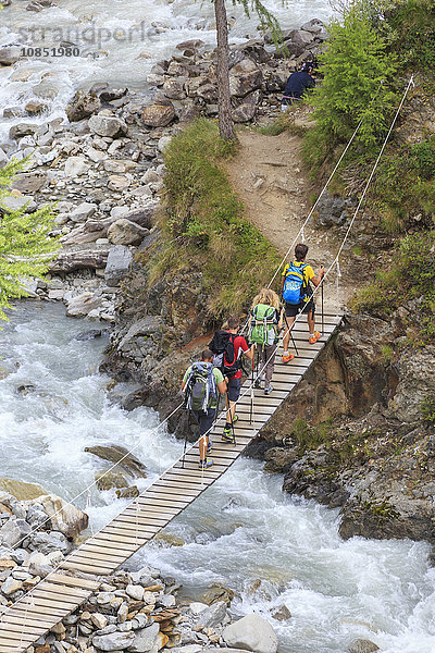 Wanderer überqueren die Holzbrücke über einen Bach im Wald  Molltal  Hochveltlin  Livigno  Lombardei  Italien  Europa