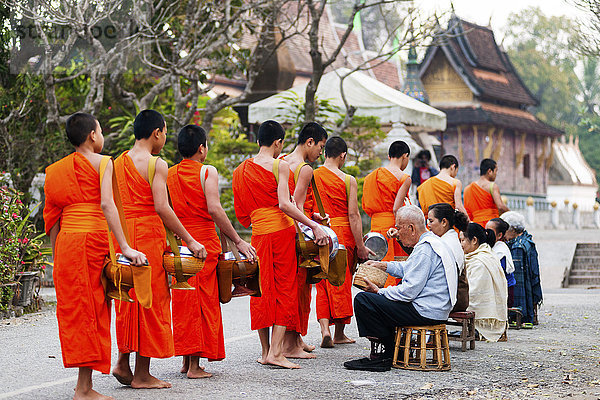 Mönche bei der Entgegennahme morgendlicher Almosen und das Kloster Xieng Thong im Hintergrund  Luang Prabang  Laos  Indochina  Südostasien  Asien