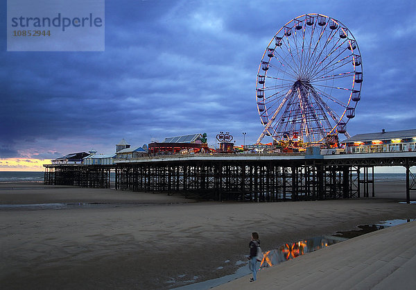 Riesenrad und Vergnügungen am Central Pier bei Sonnenuntergang mit jungen Frauen  die zuschauen  Blackpool  Lancashire  England  Vereinigtes Königreich  Europa