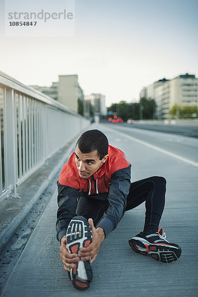 Man stretching while sitting on sidewalk