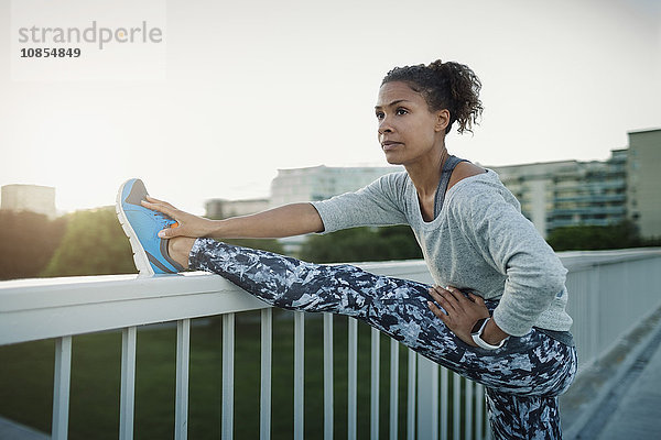 Woman stretching leg on railing at sidewalk