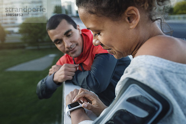 Man looking at friend using smart watch while standing by railing at sidewalk