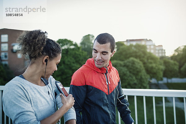 Man looking at woman using smart phone armband while walking at sidewalk