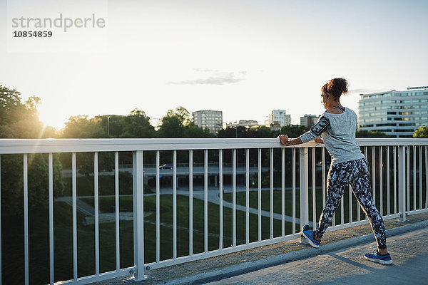 Woman exercising on railing at sidewalk