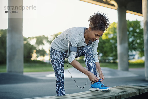 Woman tying shoelace on bench while standing at park