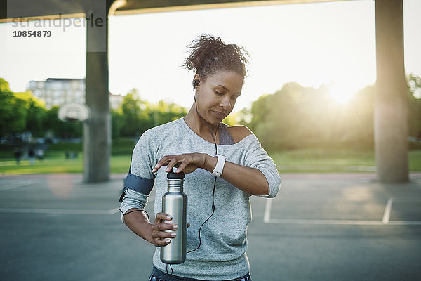 Woman checking time on smart watch while holding water bottle on street