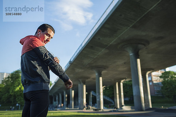 Low angle view of man touching arm band while standing against bridge