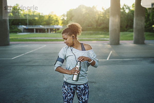 Woman holding water bottle looking down while standing on street