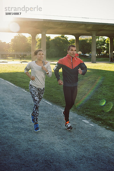 Friends jogging on street against bridge on sunny day