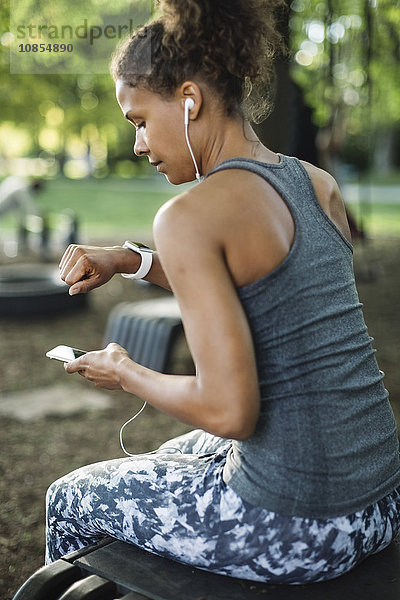 Woman using smart phone and looking at wristwatch in park