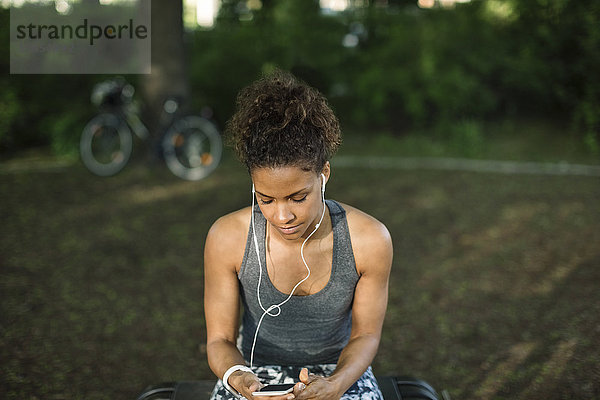 Close-up of woman sitting on bench listening music in park