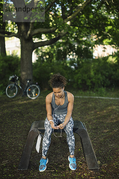 Woman sitting on bench listening music in park