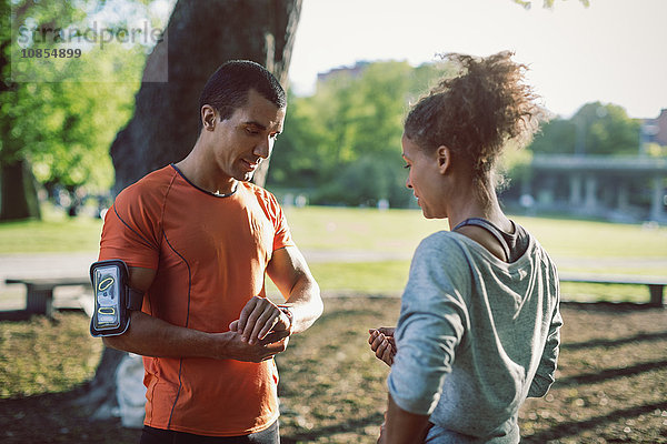 Man showing wristwatch to female friend while standing in park