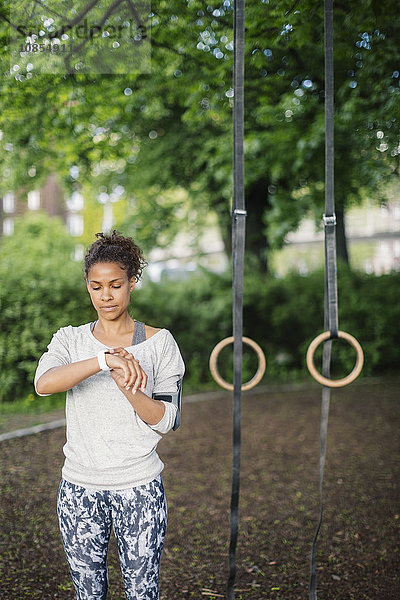 Woman using smart watch standing against gymnastic rings in park