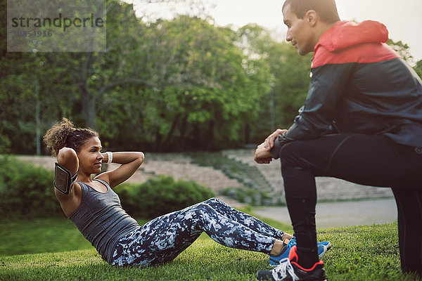 Man kneeling and looking at woman doing sit-ups on field