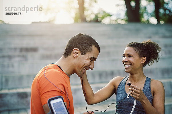 Smiling woman putting headphones on man at steps