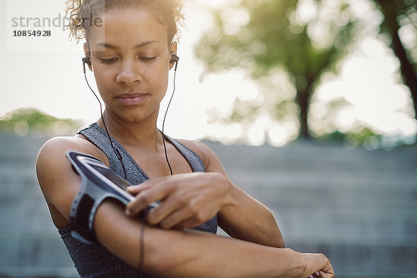 Woman using smart phone armband while standing at park