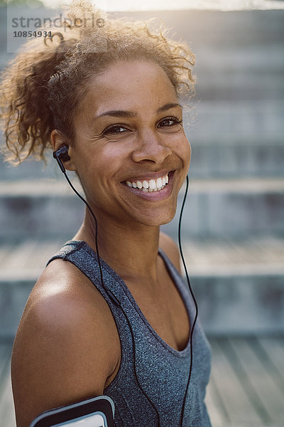 Portrait of smiling woman wearing headphones and standing at park