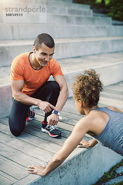 Man showing smart watch to female friend doing push ups