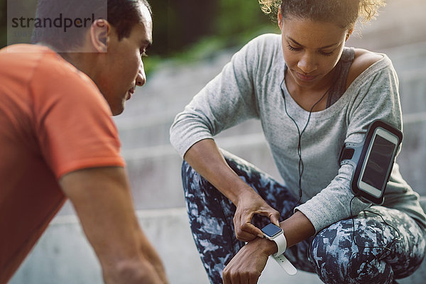 Woman looking at smart watch while friend doing push-ups