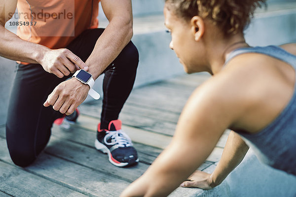 Man using smart watch while female friend doing push ups