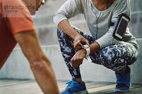 Woman using smart watch while friend doing push-ups on steps