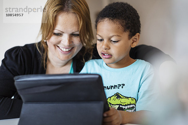 Happy mother using digital tablet with son at home