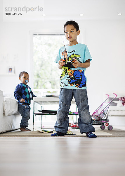 Full length of boy holding remote of model airplane at home with brother in background