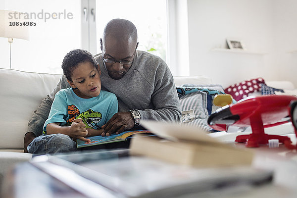Father and son reading picture book while sitting on sofa at home