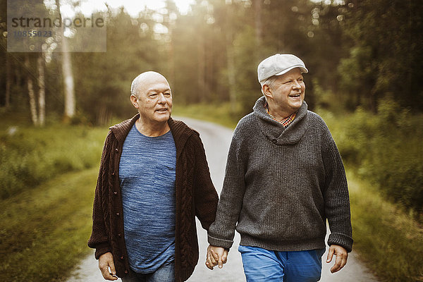 Happy gay couple looking away while walking on road amidst trees