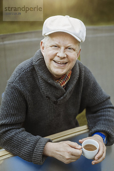 Portrait of happy man holding coffee cup while sitting at table outdoors