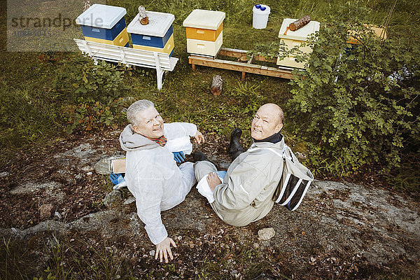 High angle portrait of happy beekeepers relaxing on field