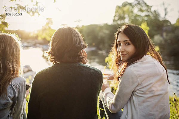 Rear view portrait of female teenager sitting with friends at lakeshore