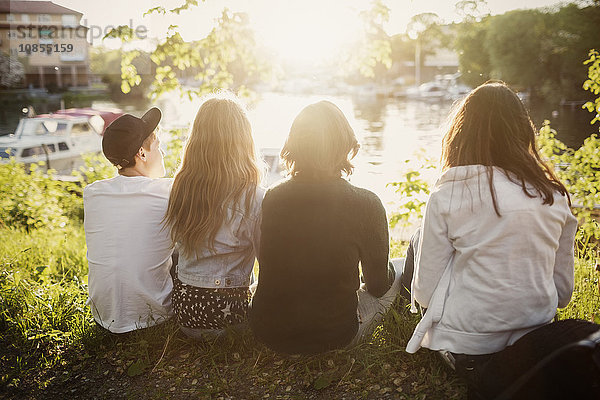 Rear view of teenagers sitting at lakeshore